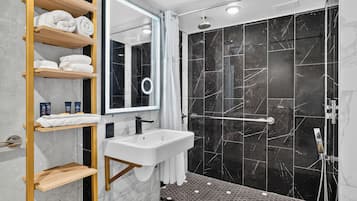 A modern bathroom with a glass-enclosed shower, marble walls, and wooden shelves with towels.