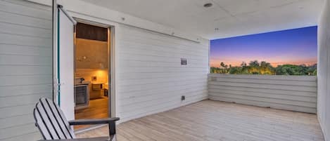 A balcony with a wooden floor, a chair, and a view of a sunset over a landscape.