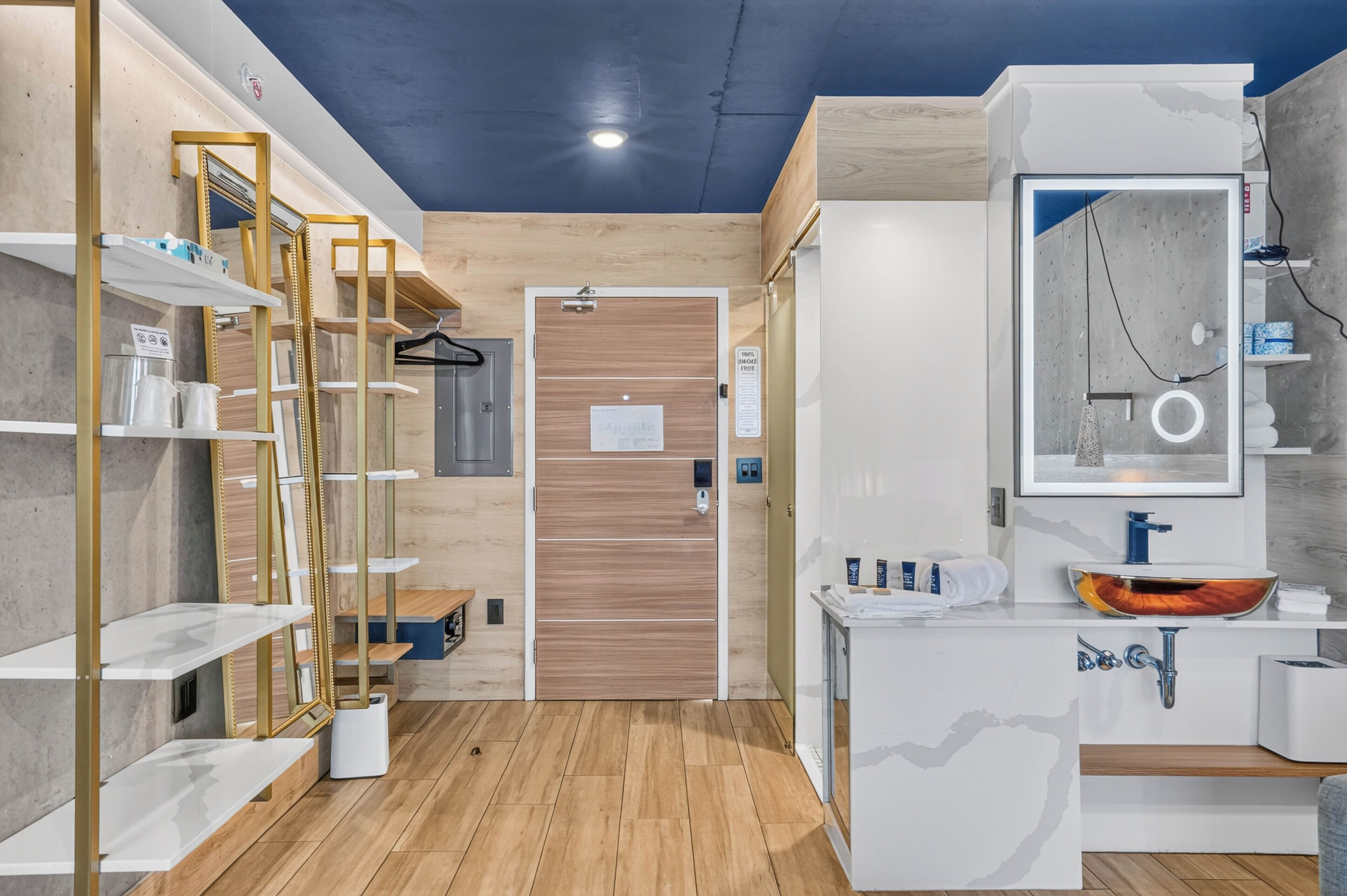 A modern bathroom with a wooden door, a mirror with a circular frame, and a sink with a unique basin design.