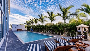 A swimming pool with lounge chairs, palm trees, and a building with large windows.