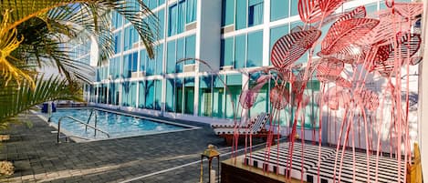 A modern hotel with a swimming pool, outdoor seating, and decorative metal plants.