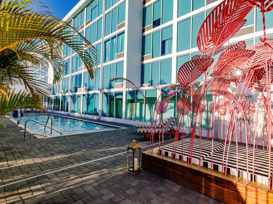 A modern hotel with a swimming pool, outdoor seating, and decorative metal plants.