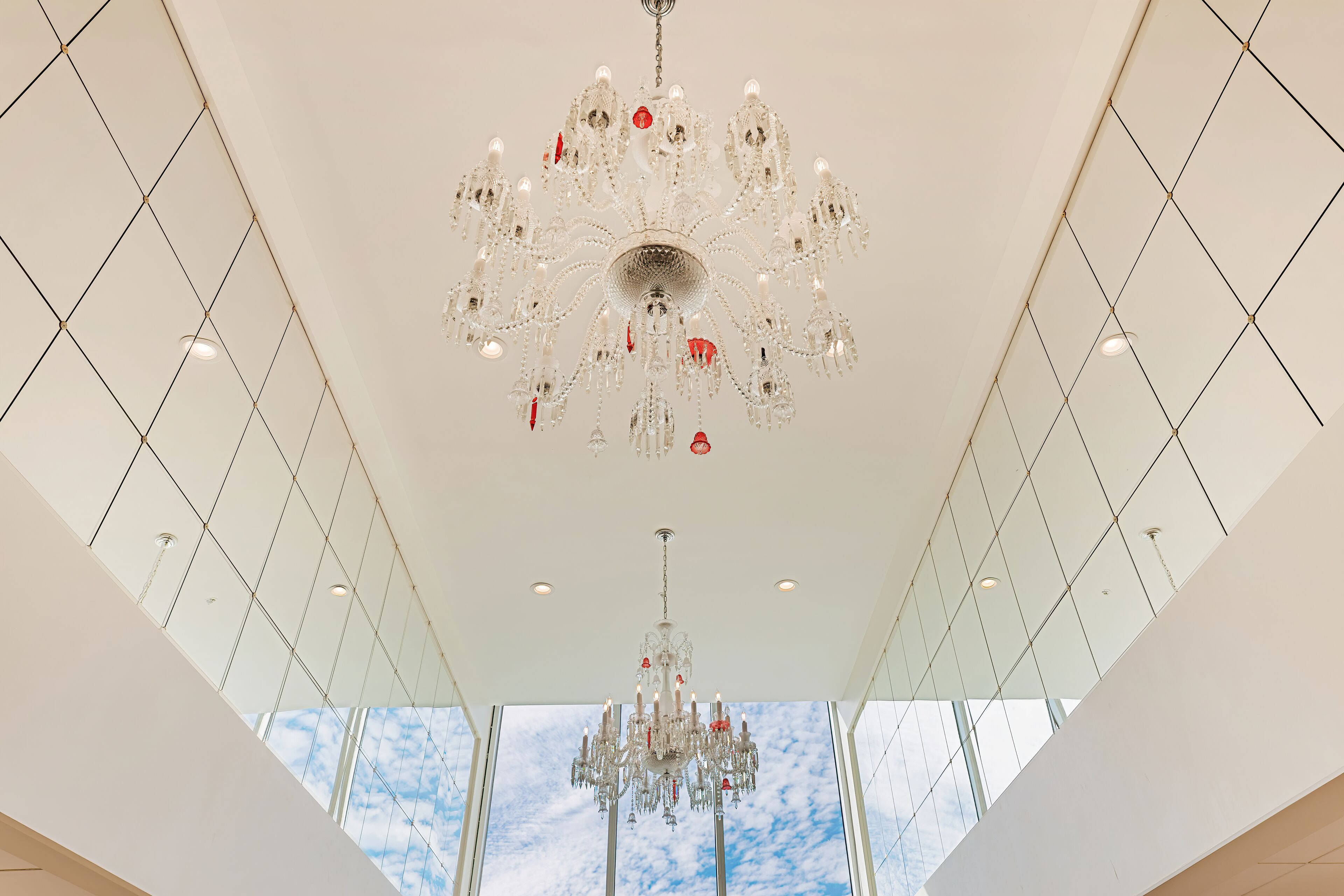 A modern interior with a large, ornate chandelier and a high ceiling with glass panels.