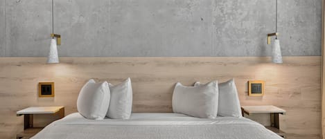 Un dormitorio moderno con una cama grande, dos mesitas de noche y una pared de hormigón con luces colgantes.