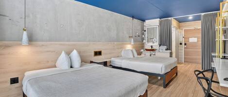 A modern hotel room with two beds, a wooden floor, a concrete accent wall, and a large mirror.