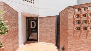 A narrow brick corridor with a tiled floor, a door marked with the letter 'D', and a brick wall with a pattern of holes.