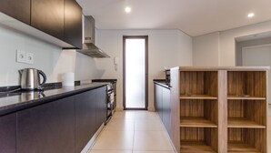 A modern kitchen with dark cabinets, a stainless steel kettle, and a wooden shelving unit.