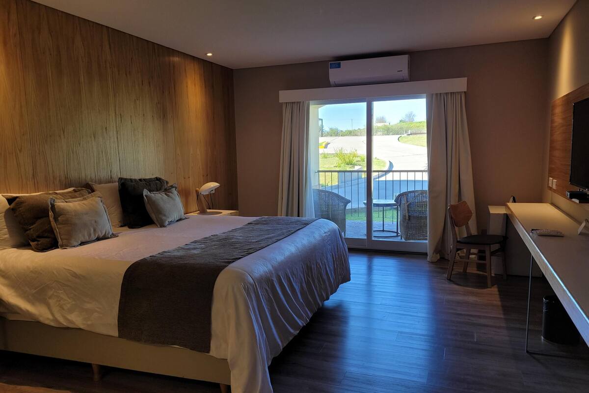 A modern hotel room with a large bed, a desk, and a view of the outdoors.