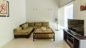 A living room with a sectional sofa, a wooden coffee table, a TV stand, and a floor lamp.