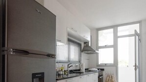 Een moderne keuken met een roestvrijstalen koelkast, witte kasten, een inbouwoven en een raam voor natuurlijk licht.