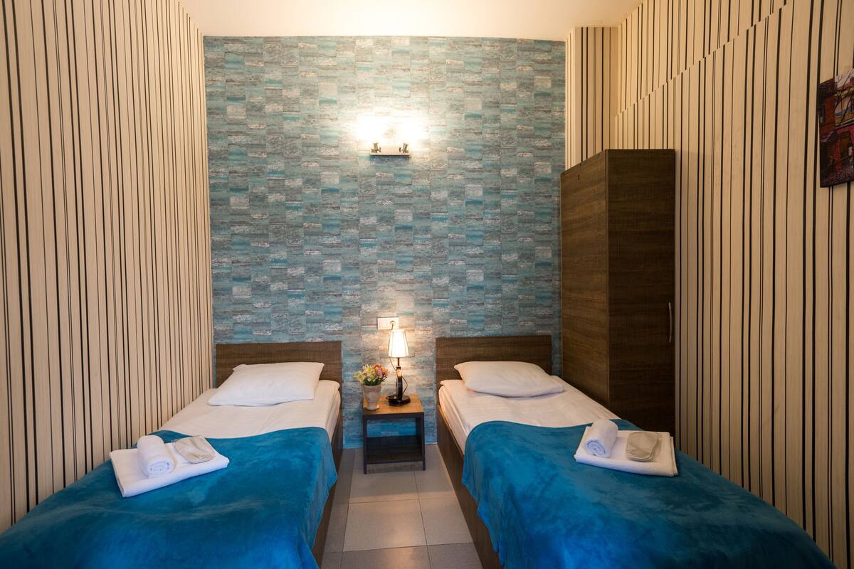 A hotel room with two beds, a nightstand with a lamp, and a decorative wall.