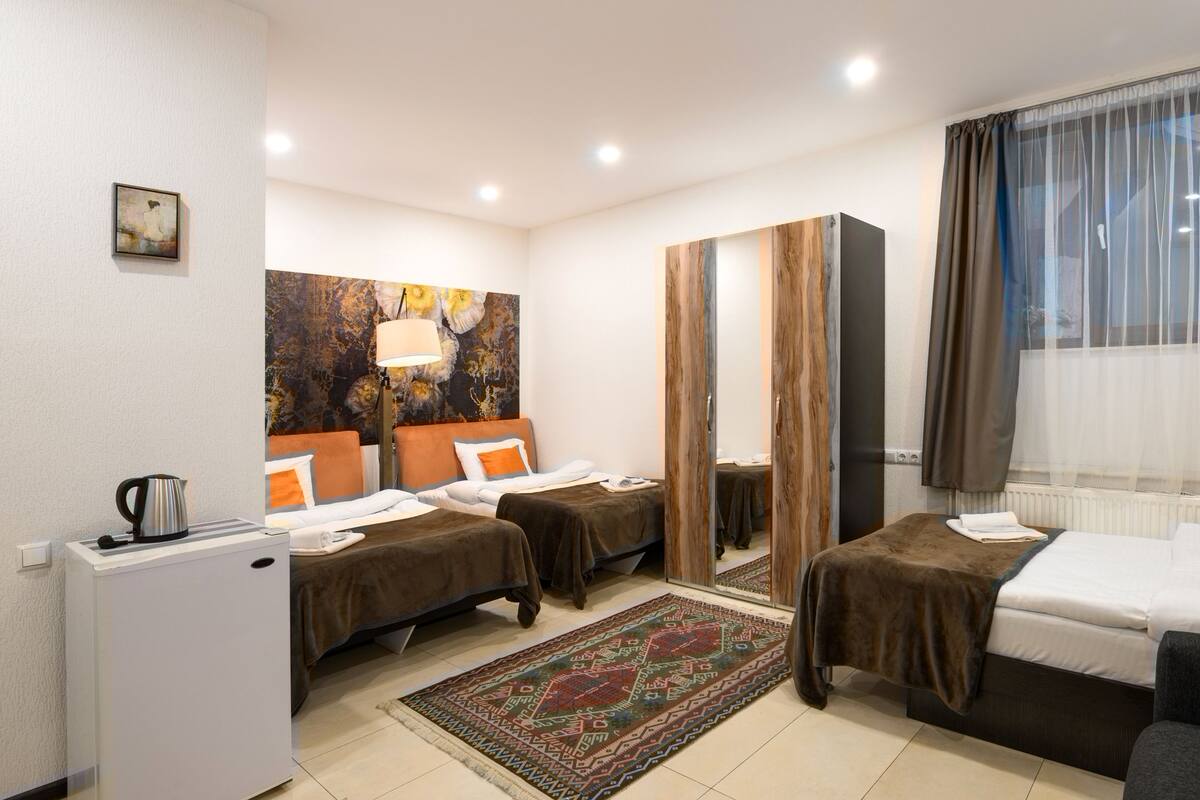 A hotel room with two single beds, a small desk with a kettle, a large mirror, and a decorative rug.