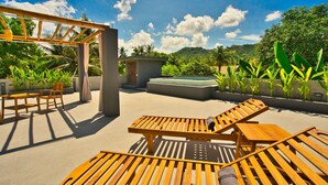 A sunlit outdoor area with wooden lounge chairs, a small table, and a pergola. - Dalai Home (Kuta)