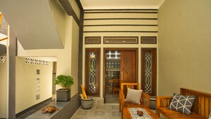 A reception area with a reception desk, a seating area with a bench and a sofa, a potted plant, and a wall with a sign. - Dalai Home (Kuta)