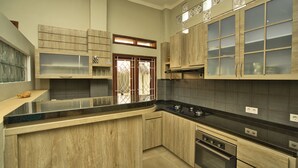 A kitchen with wooden cabinets, a black countertop, and a window with a decorative glass door. - Dalai Home (Kuta)