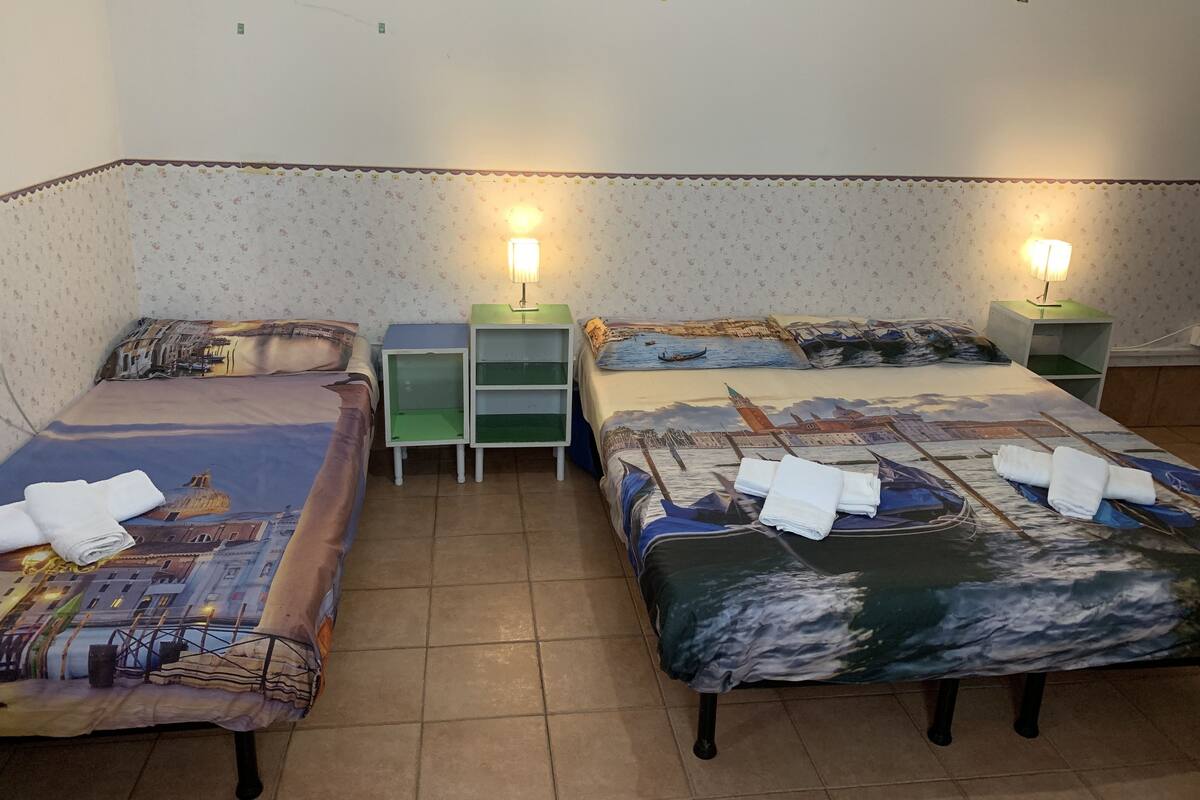 A room with two beds, each with a different patterned bedspread, flanked by nightstands with lamps.