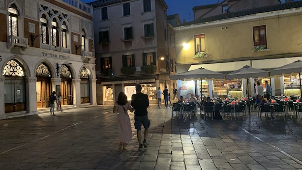 Une place historique pavée de pierres, un théâtre et des espaces de restauration en plein air dotés de parasols.