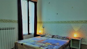 Une chambre à coucher avec un lit, deux lampes de chevet, un radiateur et une fenêtre avec des rideaux.