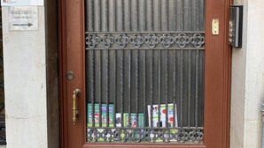 Une porte marron ornée d’une grille métallique et de motifs décoratifs en métal. Au-dessus de la porte, on peut voir une plaque portant le numéro 1954B.