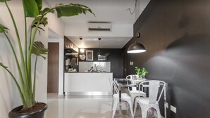 A modern kitchen with white cabinets, a central island, and a dining area with white chairs. - Modern 1 BR Apartment (Asunción)