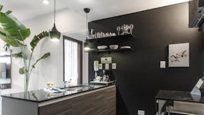 A modern kitchen with a dark backsplash, a central island, pendant lighting, and a large plant. - Modern 1 BR Apartment (Asunción)