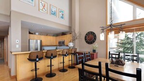 A modern kitchen with wooden cabinets, a stainless steel refrigerator, and a bar area with stools. - Overlooking Golf Course & Valley Trail, Parking (Whistler)
