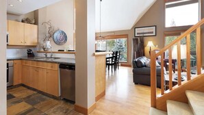 A spacious kitchen with wooden cabinets, a dining area with a table and chairs, and a staircase leading to a living area with a sofa and a lamp. - Overlooking Golf Course & Valley Trail, Parking (Whistler)