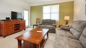Un salon comprenant un meuble de rangement en bois pour appareils multimédias, un canapé gris, un fauteuil assorti et une table basse en bois.