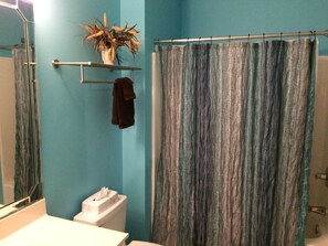 A bathroom with a blue wall, a shower curtain, a towel rack with a towel, and a toilet.