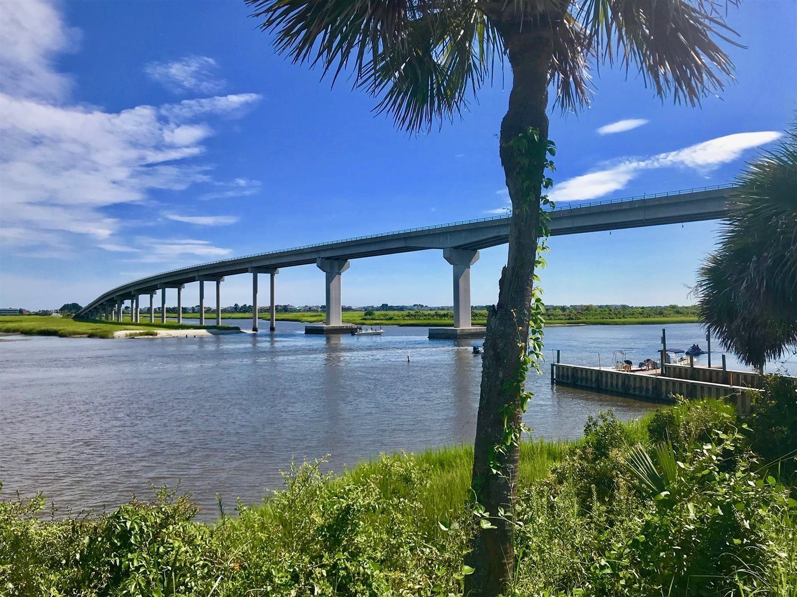 A bridge over a river with a dock and greenery in the foreground.