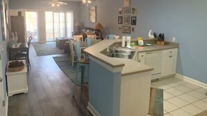 A spacious kitchen with a central island, a dining area with chairs, and a living room with a sofa and a coffee table. - 3709 Champions (Sunset Beach)