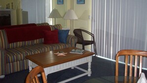 A living room with a striped sofa, a wooden coffee table, and a wicker chair. - 202 Colony II (Sunset Beach)