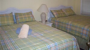 A room with two beds, each with plaid bedding and pillows. There is a lamp on a bedside table. - 202 Colony II (Sunset Beach)