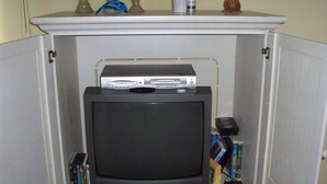 A cabinet with a television and DVD player on top, surrounded by books. - 202 Colony II (Sunset Beach)