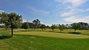 Un parcours de golf doté d’une pelouse bien entretenue, d’arbres et de bunkers de sable.