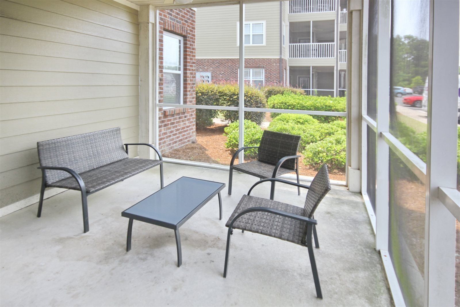 A covered patio with two sofas and a table, overlooking a brick building and a street.
