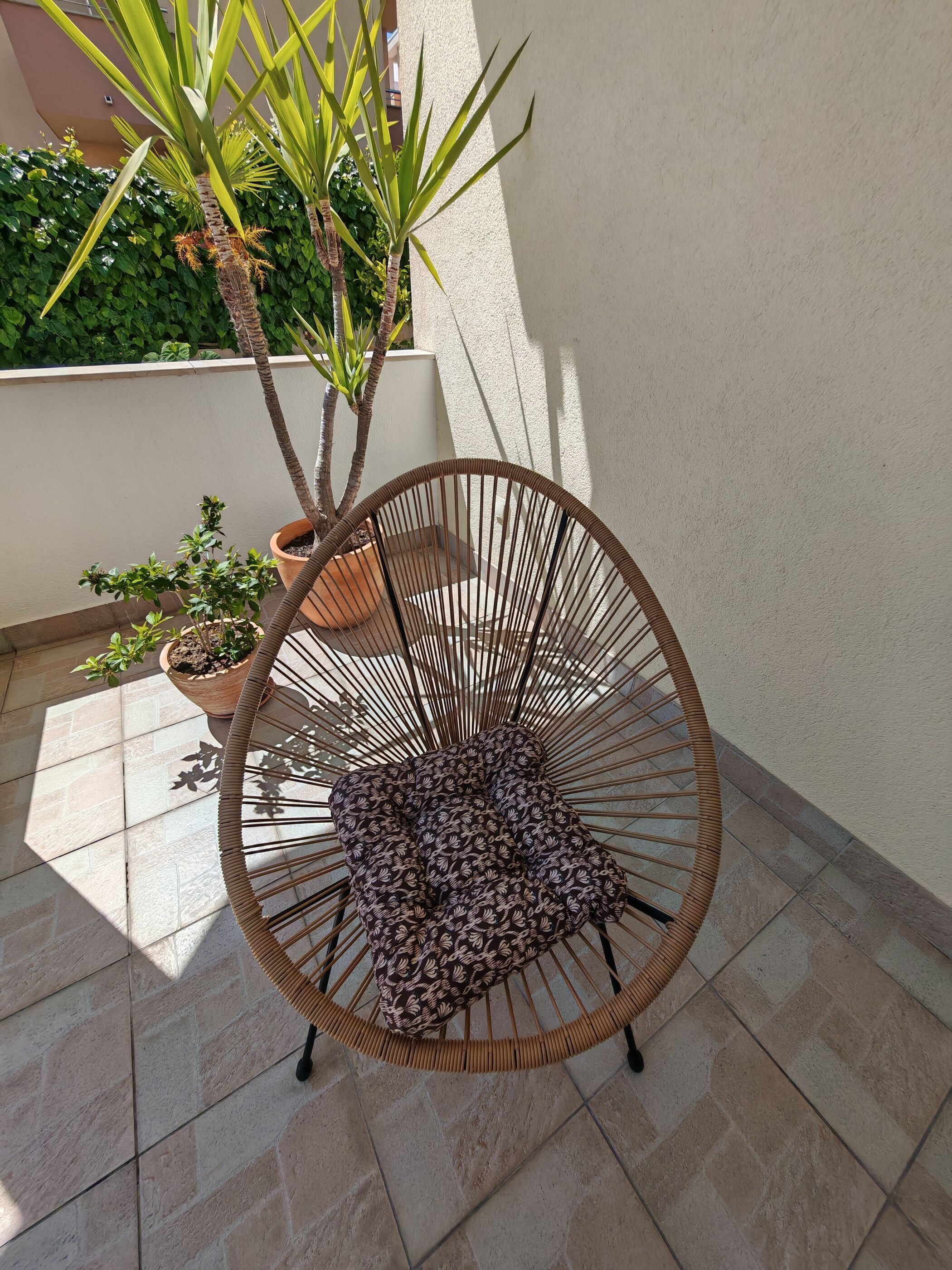A wicker chair with a patterned cushion, a potted plant, and a tiled floor.