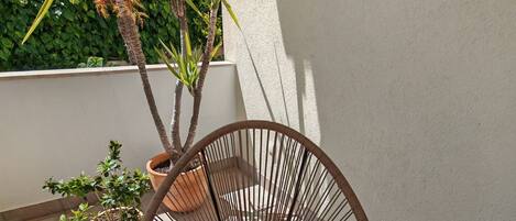 A wicker chair with a patterned cushion, a potted plant, and a tiled floor.