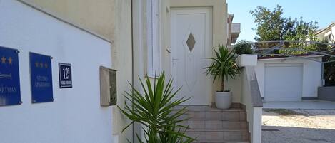 Un edificio con fachada blanca, una puerta y una escalera que conduce a un garaje. Hay dos macetas con plantas y un letrero que indica un estudio.