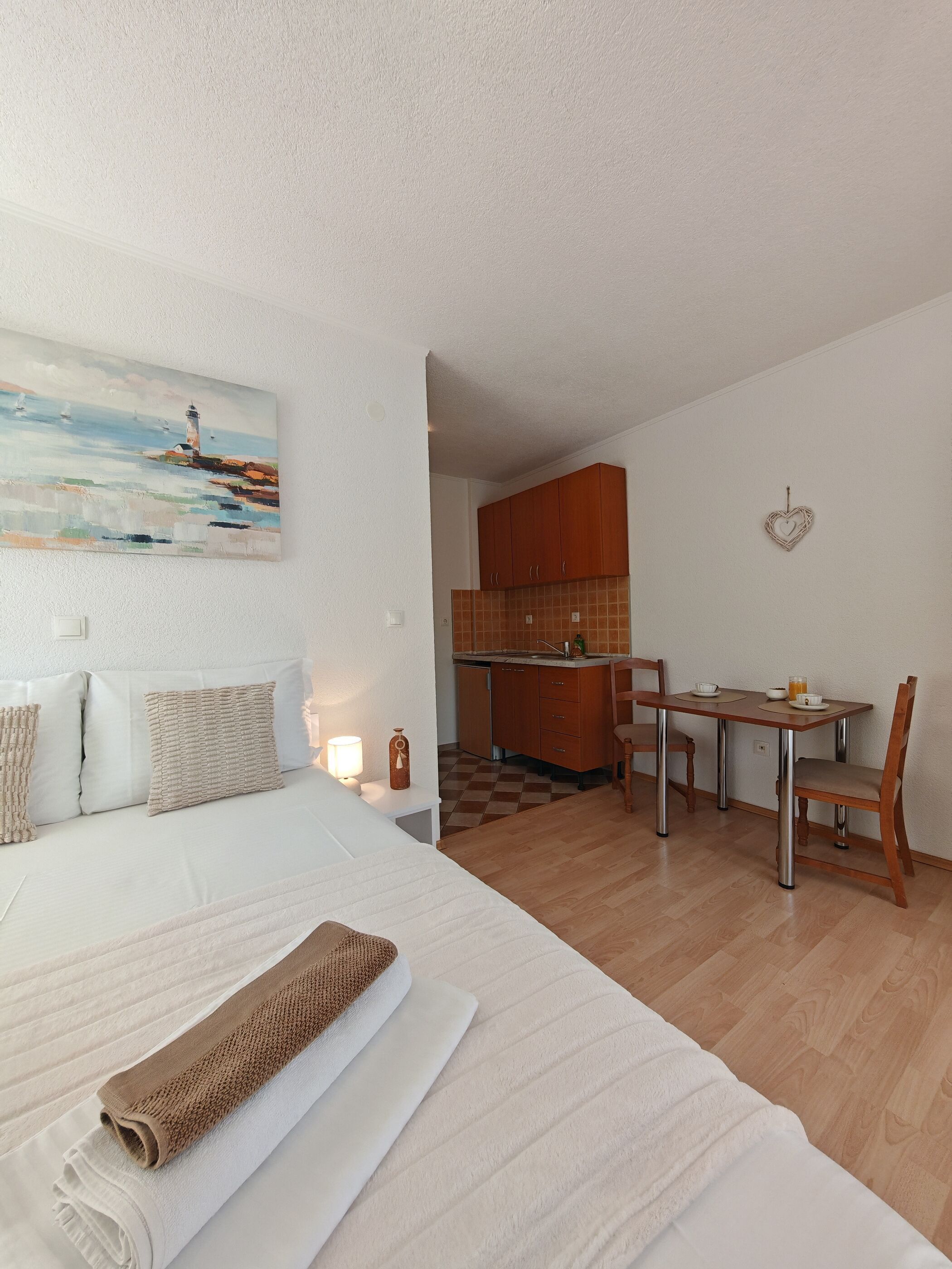 Ein Schlafzimmer mit einem Bett, einem Nachttisch, einem Gemälde und Blick zur Küche.