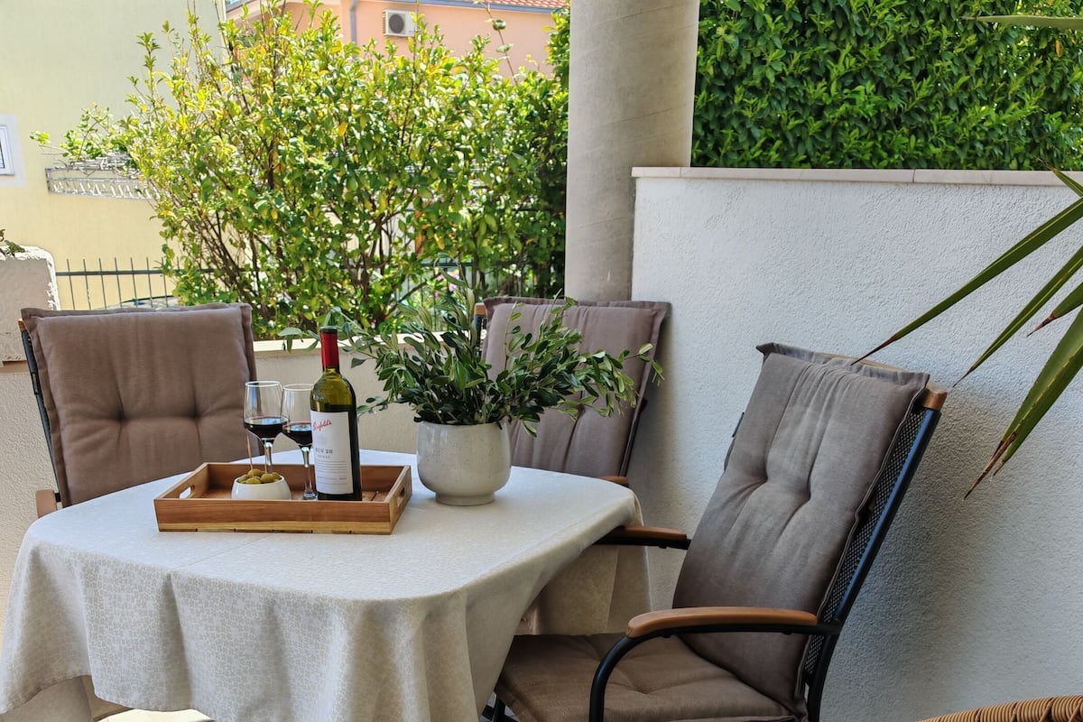 Une terrasse avec une table dressée pour deux personnes, une chaise en osier et une plante en pot.