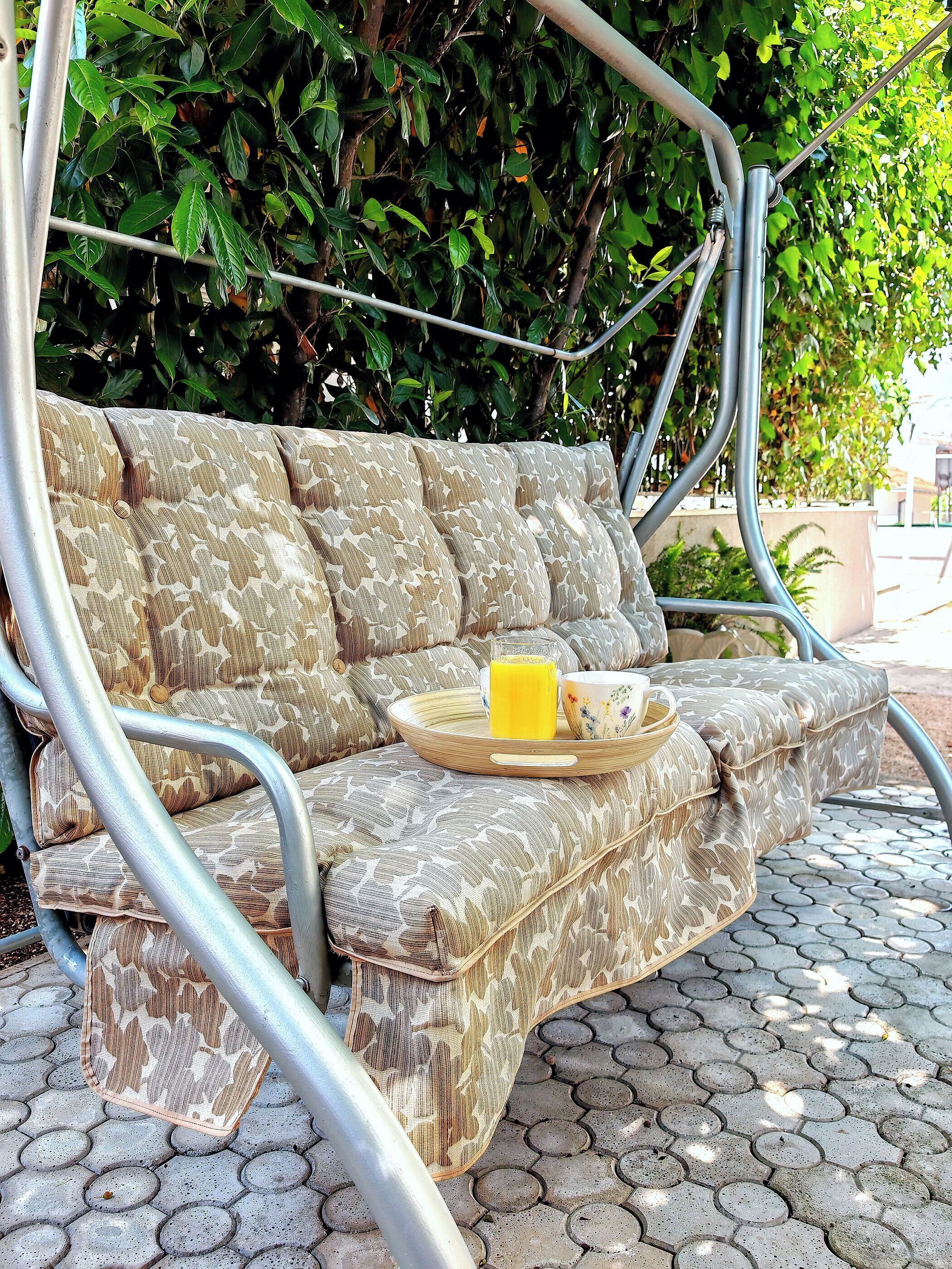A metal-framed outdoor sofa with a patterned fabric, a tray with a glass of orange juice, and a bowl.
