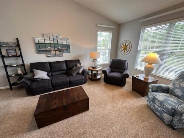 A living room with a black leather sofa, a patterned armchair, a wooden coffee table, and a side table with a lamp.