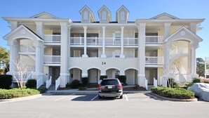 A multi-story hotel with a symmetrical facade, balconies on each floor, and a parking lot in front. - 2407 Commons II (Calabash)