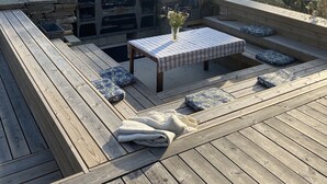 A wooden deck with a stone fire pit, a table with a checkered tablecloth, and a vase with flowers. - Modern house with stunning ocean view and heated private pool (30°) (Borgholm N)