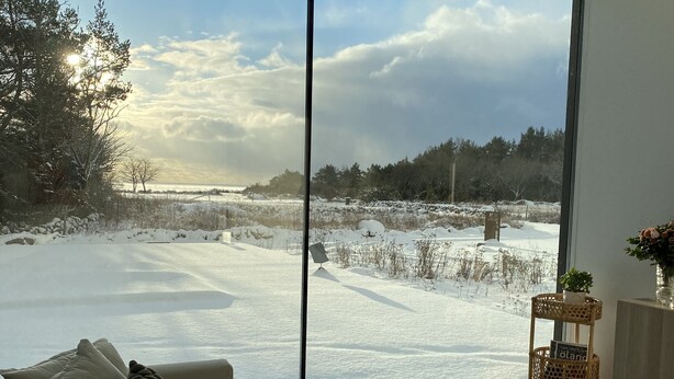 A modern living room with a large window offering a view of a snowy landscape. - Modern house with stunning ocean view and heated private pool (30°) (Borgholm N)