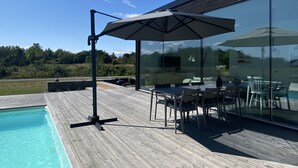 A modern outdoor deck with a pool, glass walls, and outdoor furniture. - Modern house with stunning ocean view and heated private pool (30°) (Borgholm N)