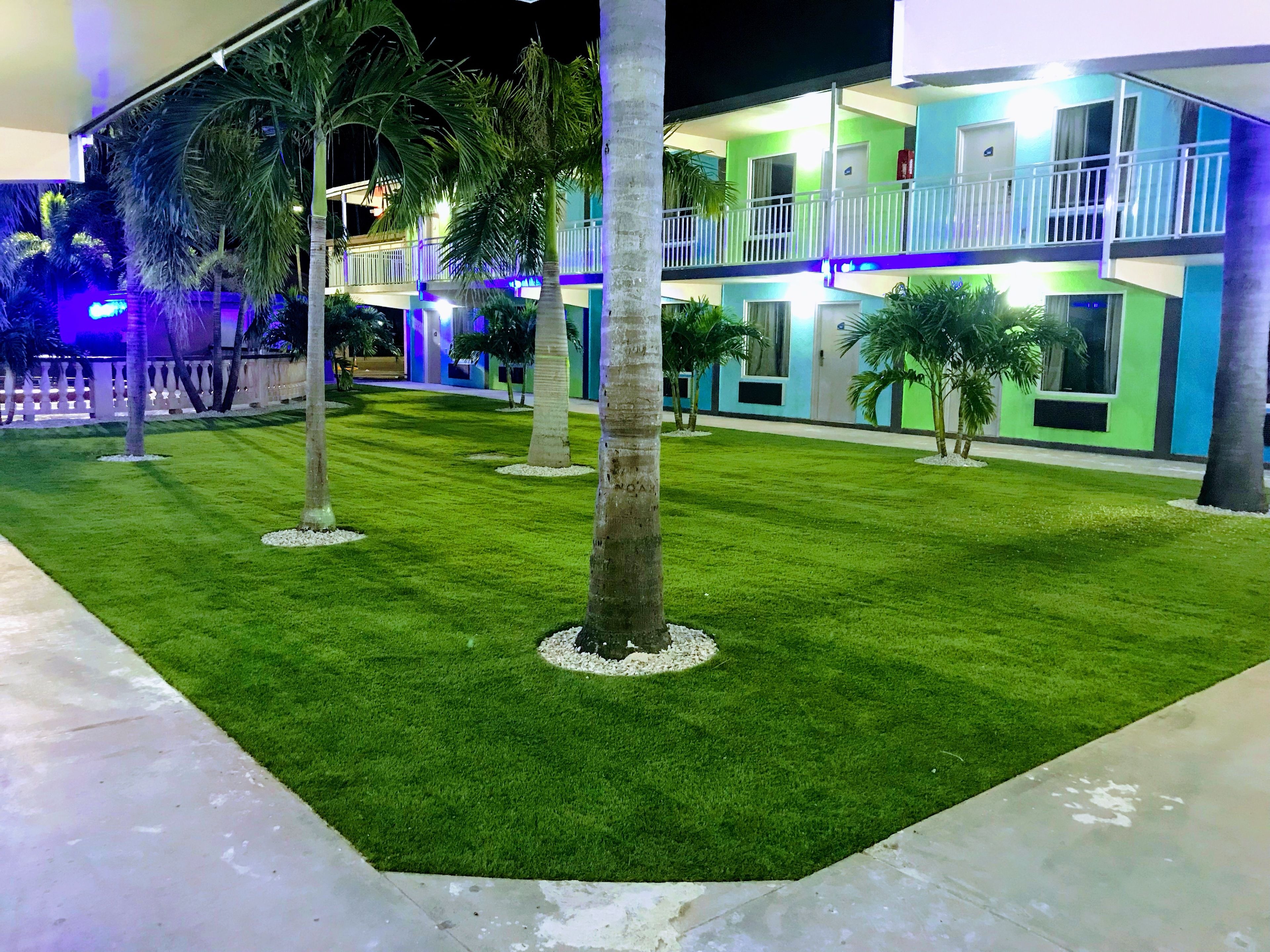 A hotel with a well-maintained lawn, palm trees, and a balcony with a railing.