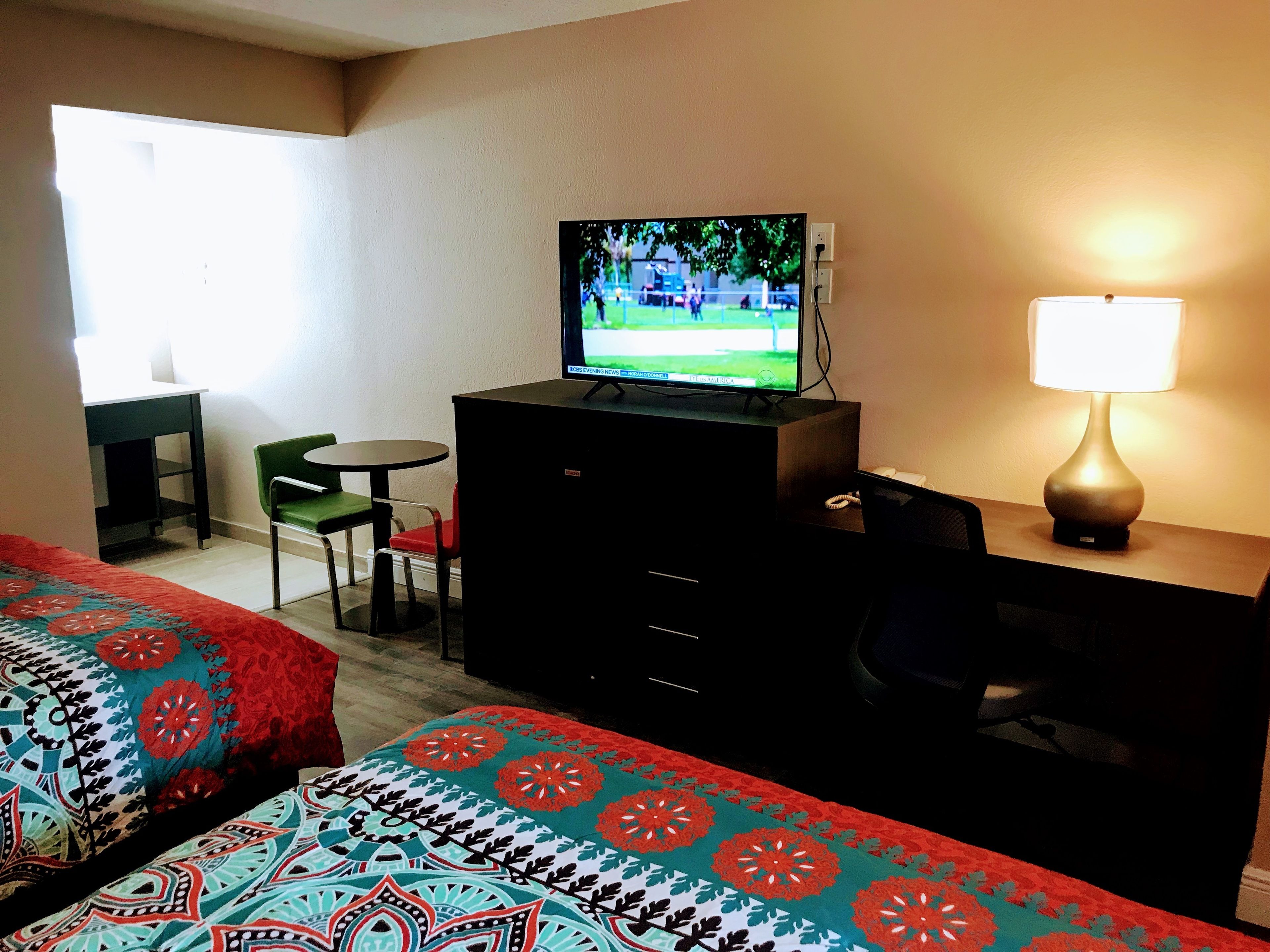 Una habitación de hotel con una cama, un televisor en una cómoda, un escritorio con una silla y una lámpara.