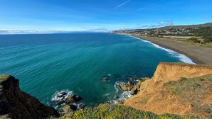 Eine Küstenlandschaft mit freiem Blick auf den Ozean, einem Sandstrand und einer Stadt in der Ferne.